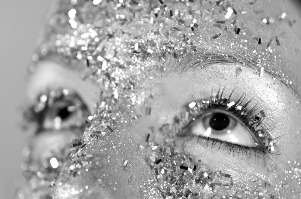 Gros plan sur un œil maquillé de paillettes argentées, en noir et blanc