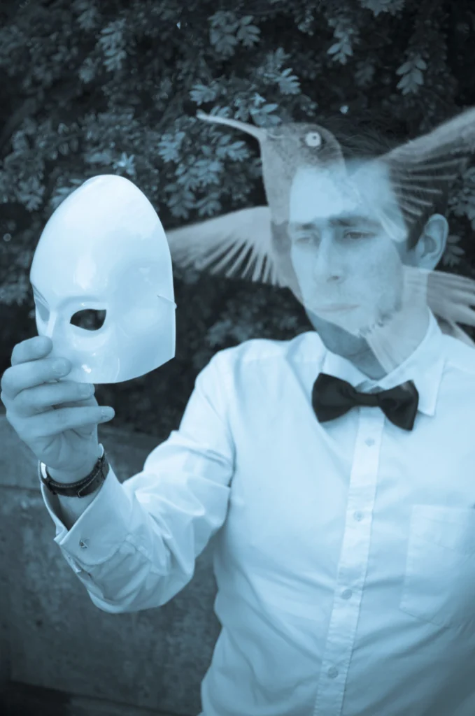 Homme en nœud papillon tenant un masque blanc, oiseau en surimpression