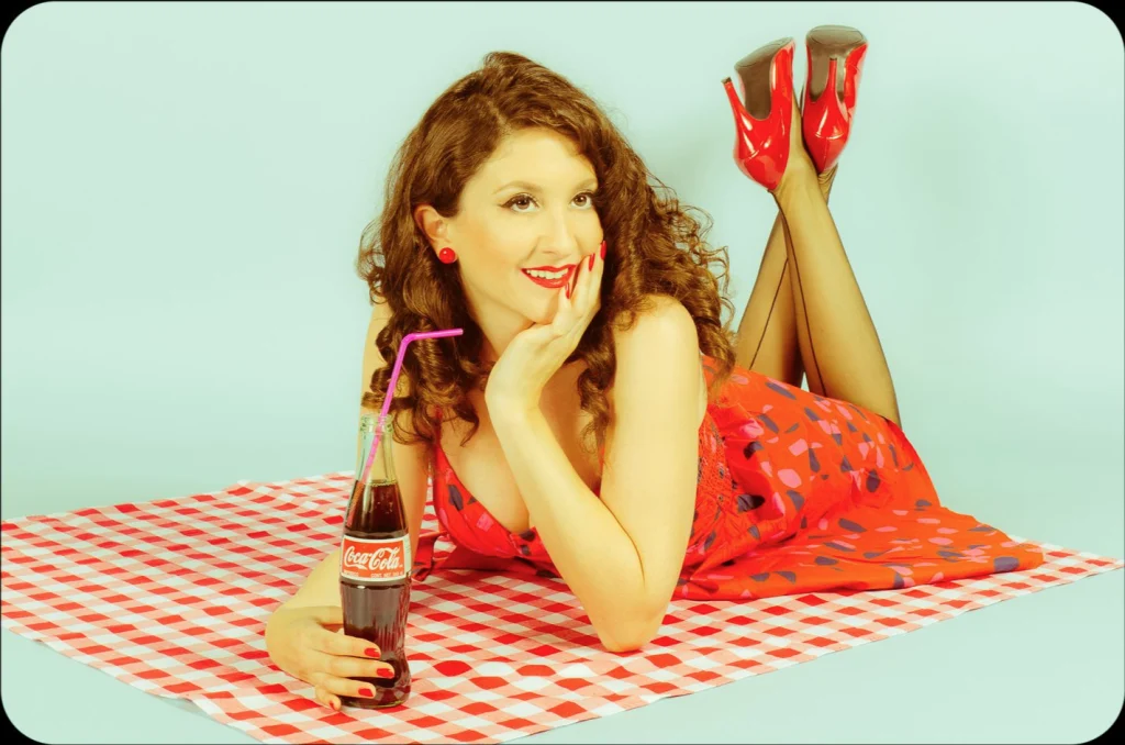 Pin-up allongée sur une nappe à carreaux rouges, une bouteille à la main