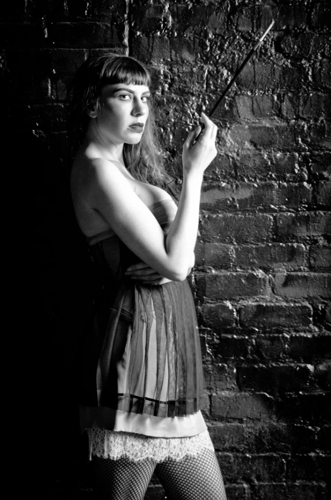 Femme au fume-cigarette en robe à franges, mur de briques