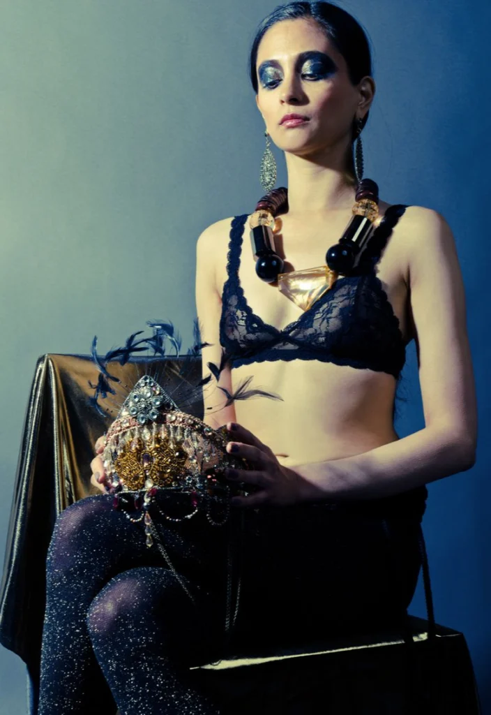 Femme assise en soutien-gorge de dentelle et colliers, tenant une coiffe dorée