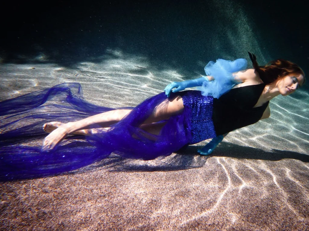 Femme nageant sous l'eau, un voile bleu flottant autour d'elle