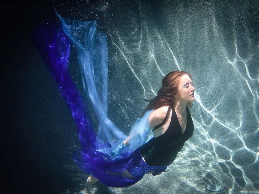Femme sous l'eau dans des reflets de lumière, traîne bleue
