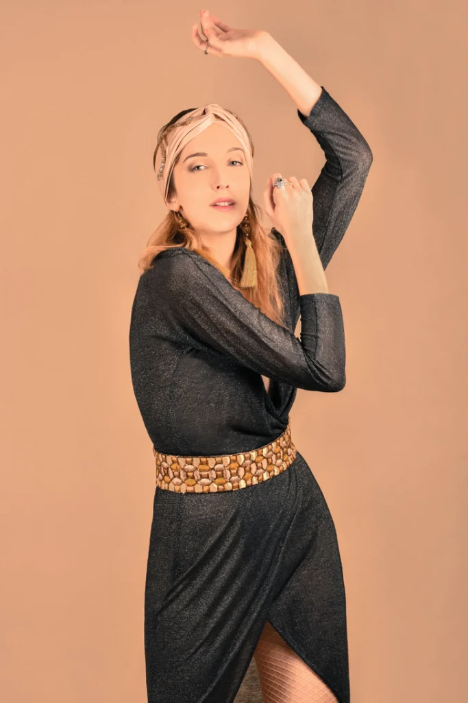Femme en robe noire, une main dans les cheveux, sur fond orange