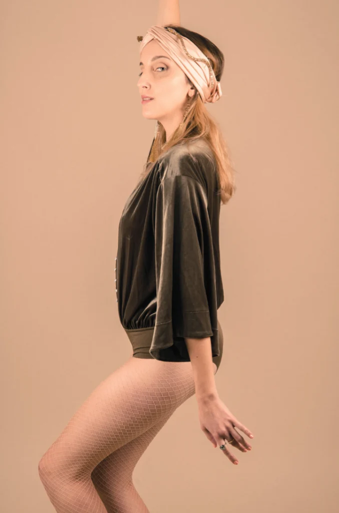 Femme de profil en blouse noire, jambes nues, sur fond orange