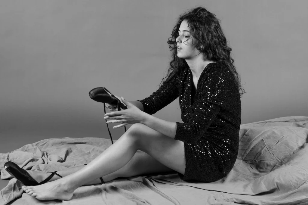 Jeune femme assise sur un lit tenant un escarpin, en noir et blanc
