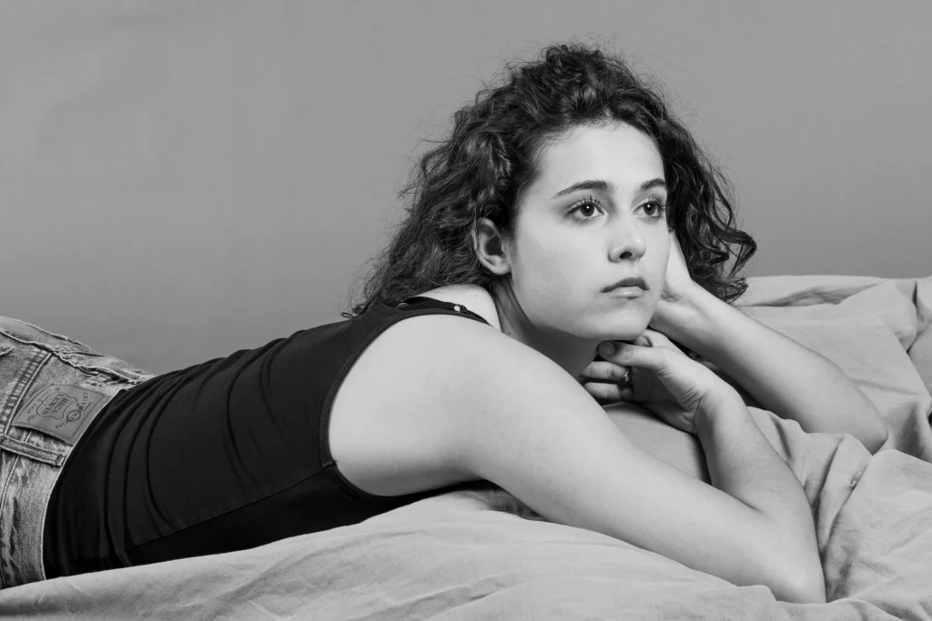 Jeune femme allongée sur des draps, le menton dans les mains, en noir et blanc