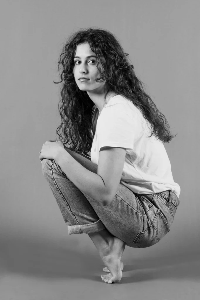 Jeune femme aux cheveux bouclés accroupie, en t-shirt blanc et jean, en noir et blanc