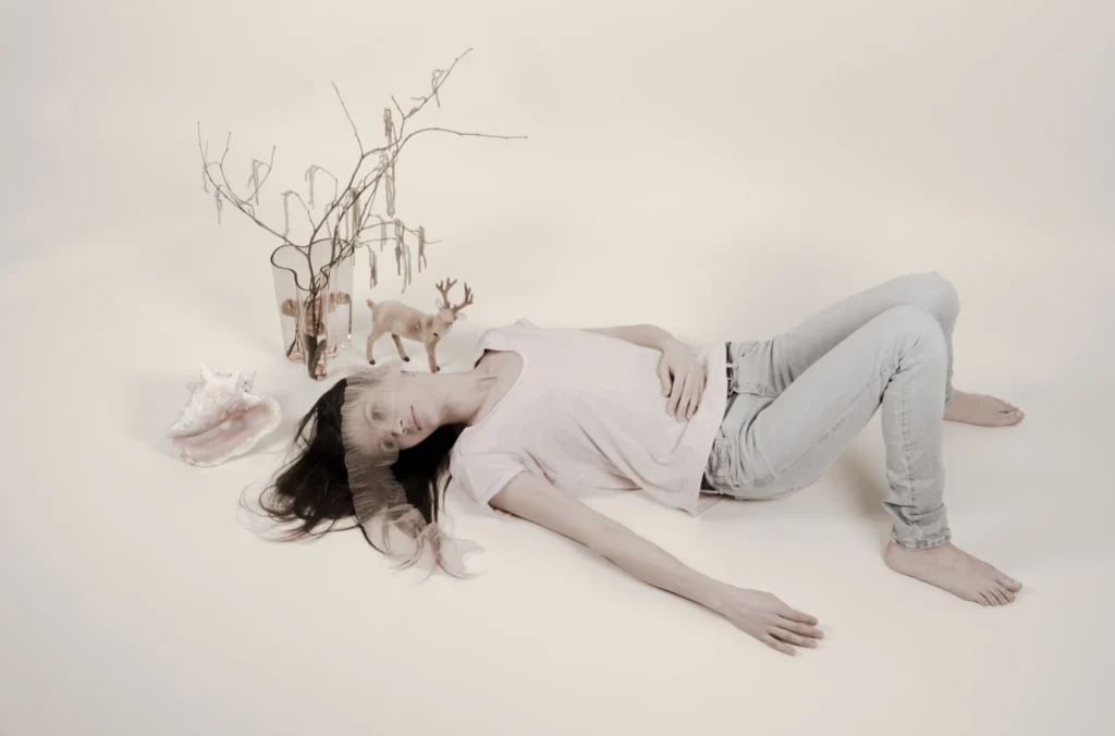 Femme allongée au sol parmi des branches et des fleurs séchées