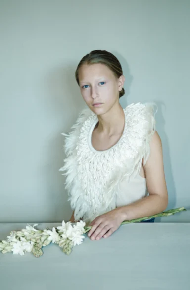 Jeune femme au col de plumes blanches, fleurs blanches posées devant elle